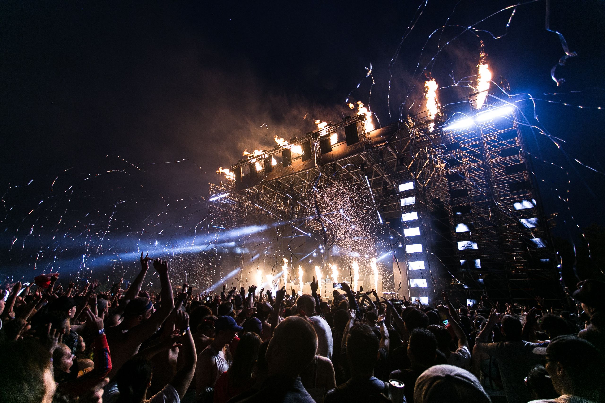 Massive concert crowd facing a giant LED stage screen at night